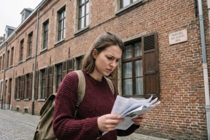 Étudiante cherchant un logement devant une façade en briques rouges typique de Lille, tenant des annonces imprimées dans la rue pavée