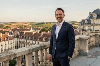 Promoteur immobilier en costume marine sur une terrasse avec vue panoramique sur les toits de Dijon et les collines viticoles de Bourgogne-Franche-Comté